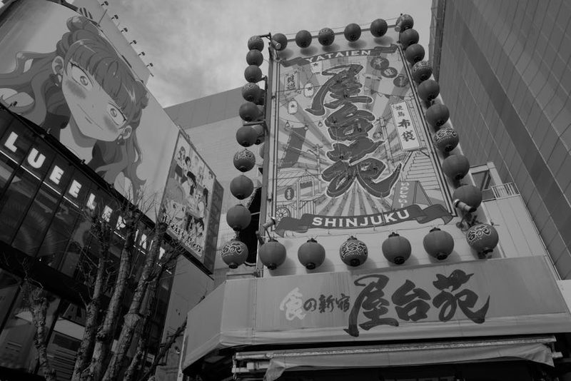 A lively urban scene in Shinjuku, Tokyo with bold, colorful signage and anime billboards during the day.