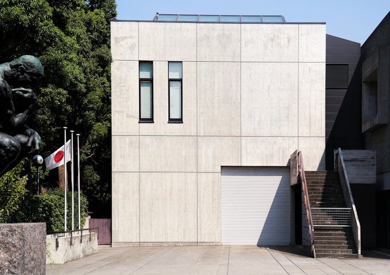 Exterior view of a modern museum building in Tokyo featuring Japanese flags and a statue.