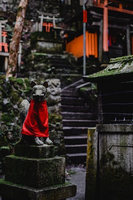 Stone fox statue with red bib at Fushimi Inari, a famous Shinto shrine in Kyoto, Japan.