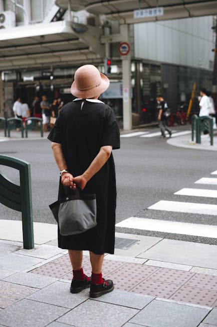 Woman in black dress with sun hat standing at a crosswalk in Kyoto. Urban scene.