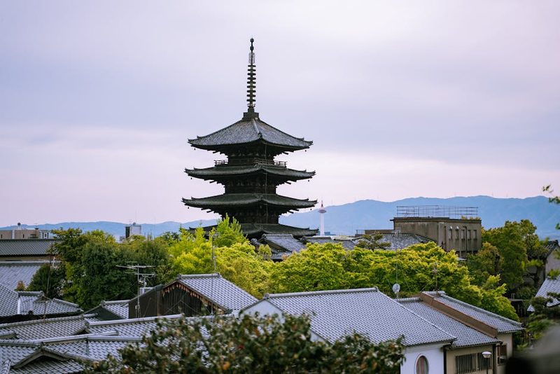 A captivating shot of Yasaka Pagoda amidst green foliage and traditional rooftops in Kyoto, Japan.