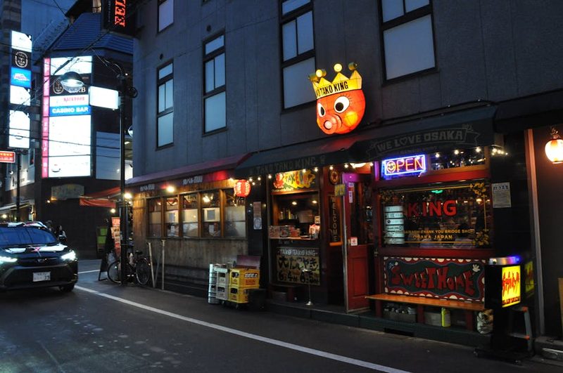 Colorful street view of Takoyaki King restaurant in Osaka at dusk, vibrant neon signs.