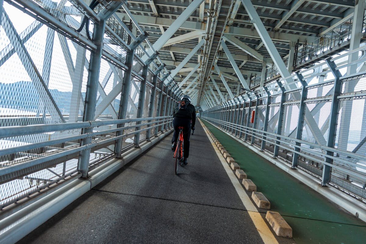 Cyclist riding through the enclosed steel framework of a Shimanami Kaido bridge with the sea visible through the structure