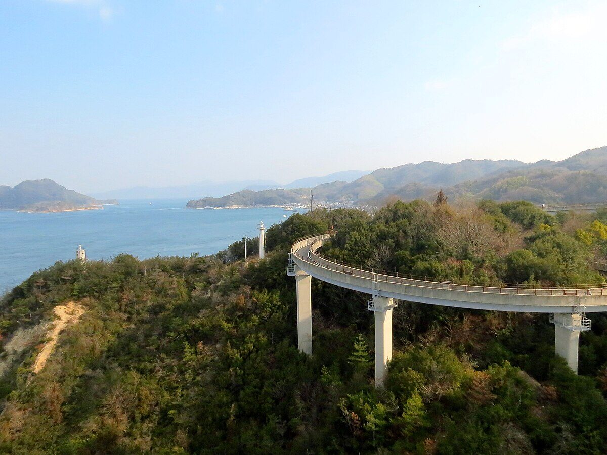 Winding concrete ramp approach leading up to a Shimanami Kaido bridge, with the dedicated cycling path clearly visible