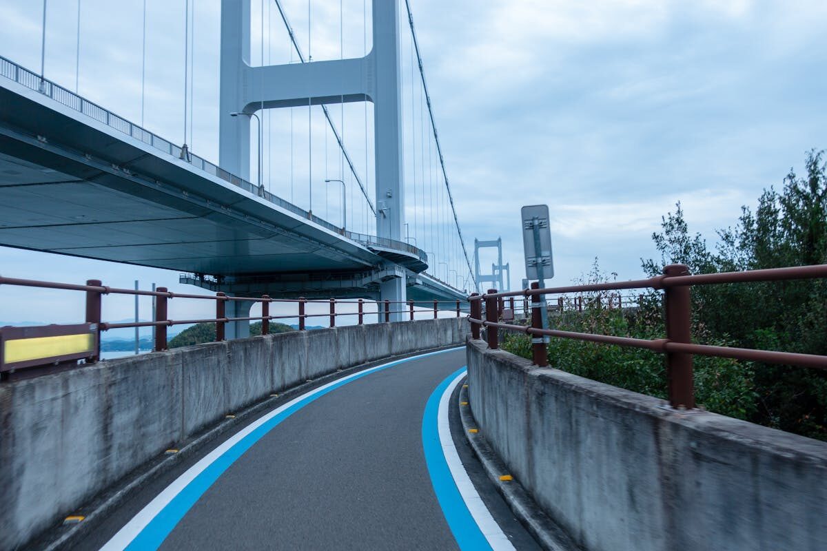 Curved cycling lane winding beneath a bridge on the Shimanami Kaido, with the sea and islands in the background