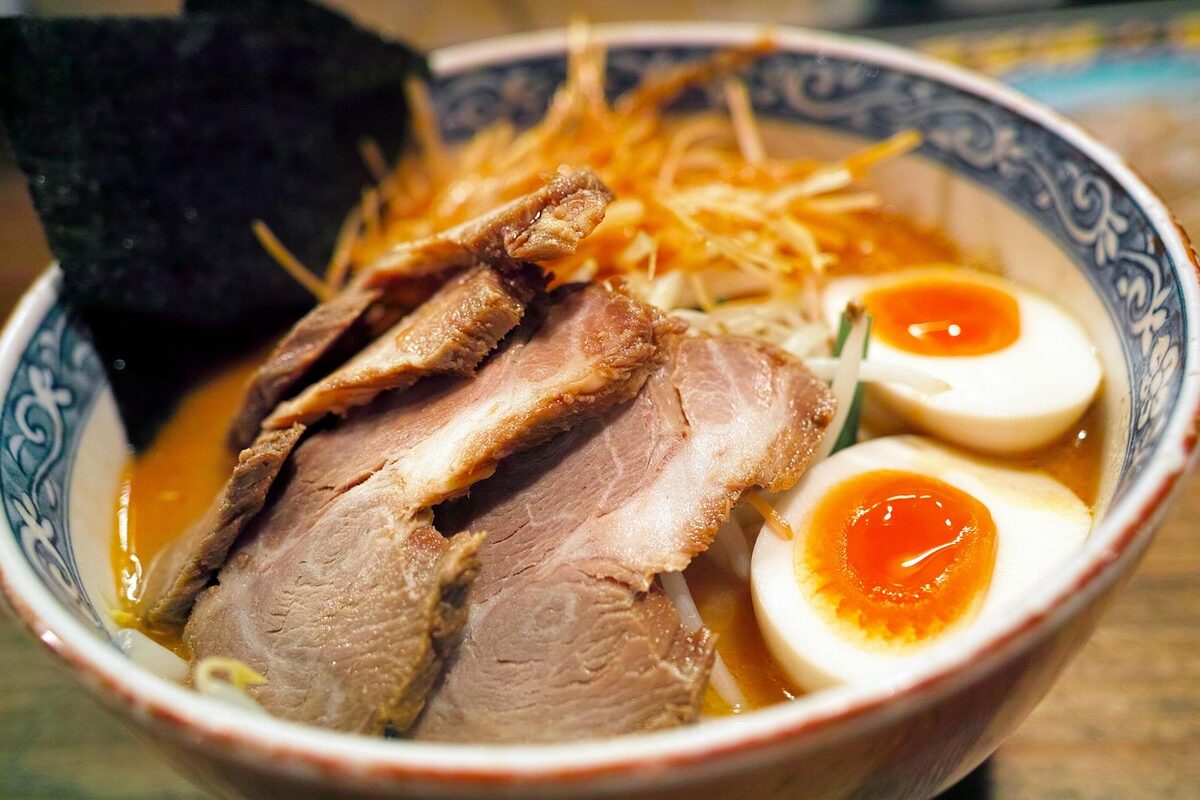 Steaming bowl of pork ramen with soft-boiled egg, nori seaweed, and sliced chashu pork in rich broth