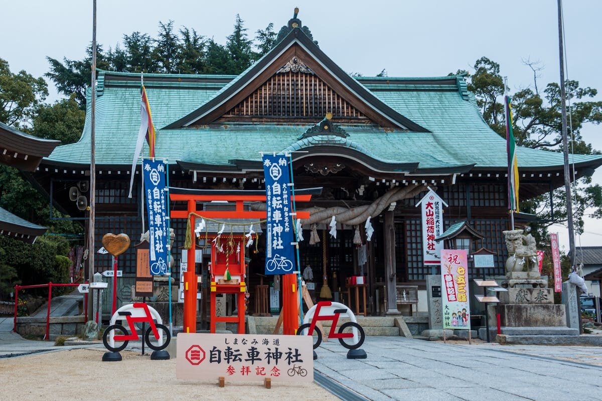 Traditional Japanese shrine entrance with stone torii gate and steps leading upward through trees in Onomichi