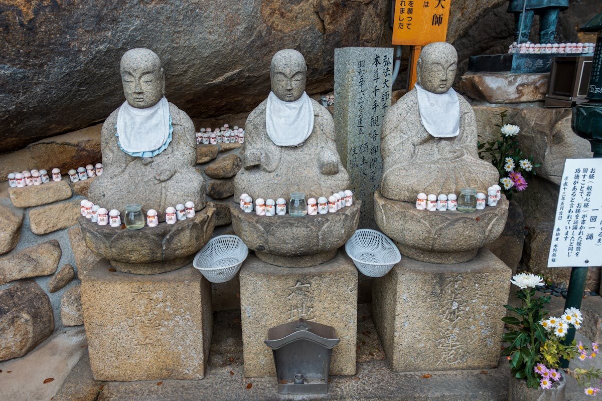Weathered stone Buddhist statues lined up at a shrine in Onomichi, Japan, surrounded by greenery