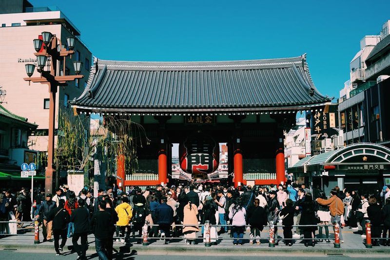 Large crowd gathers at the iconic Senso-ji Temple gate in Tokyo, Japan, under a clear blue sky.