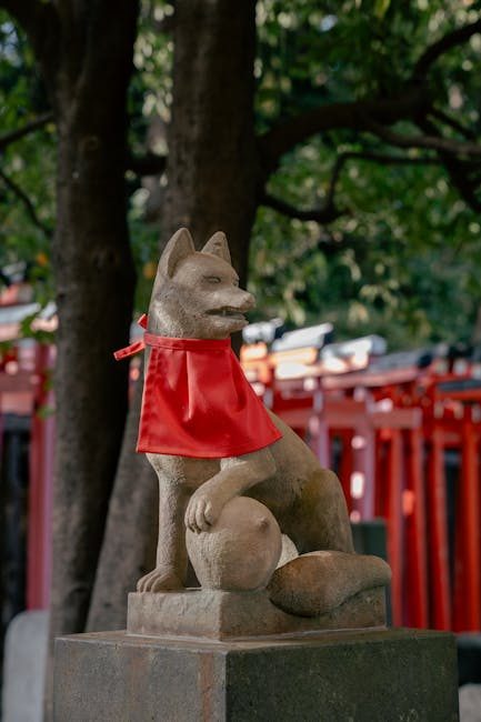 A stone fox statue with a red bib at Nezu Shrine in Tokyo, symbolizing protection.