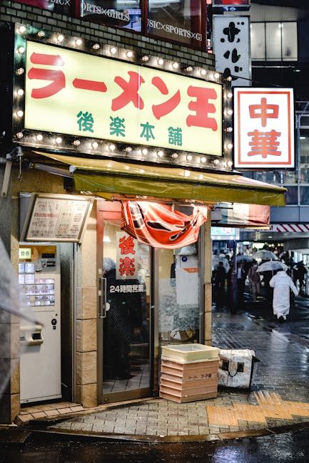 A lively Tokyo street scene with people passing by a ramen shop glowing on a rainy night.