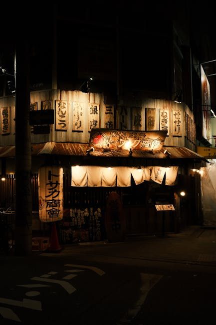 A nighttime view of a traditional Japanese izakaya with warm lights and hanging signs.