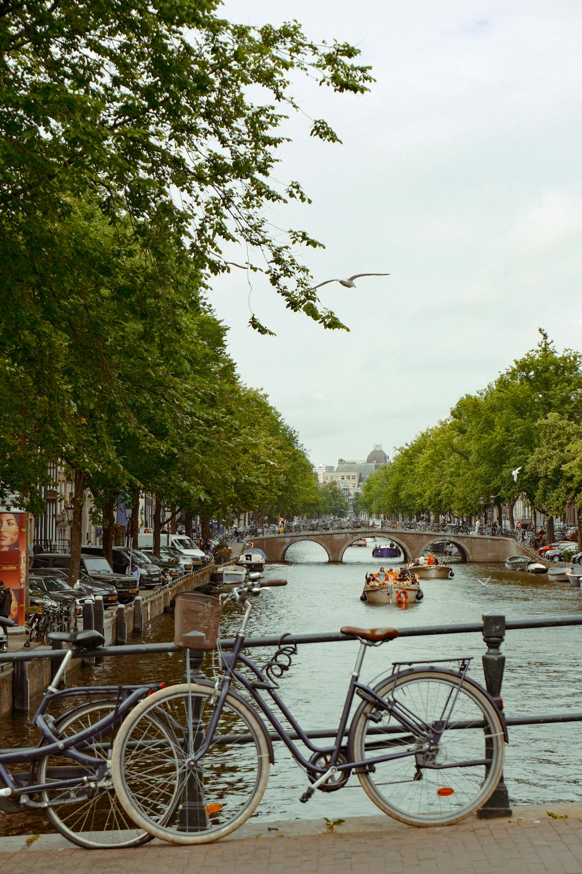 Bikes lined along an Amsterdam canal bridge with houseboats below