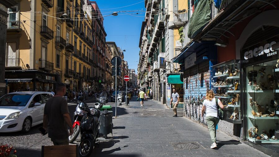 A sunny street in Naples old town lined with shops and pedestrians