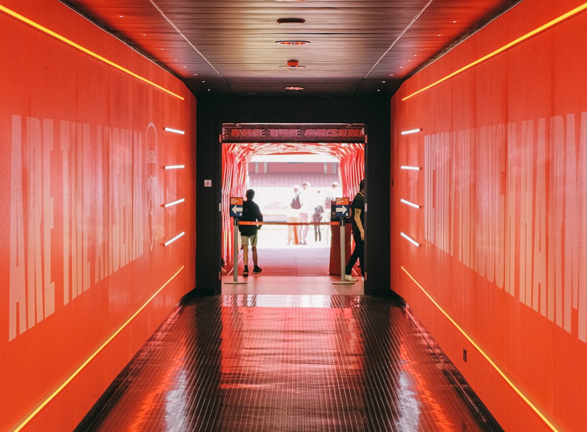 Players tunnel inside a football stadium with red walls leading to the pitch