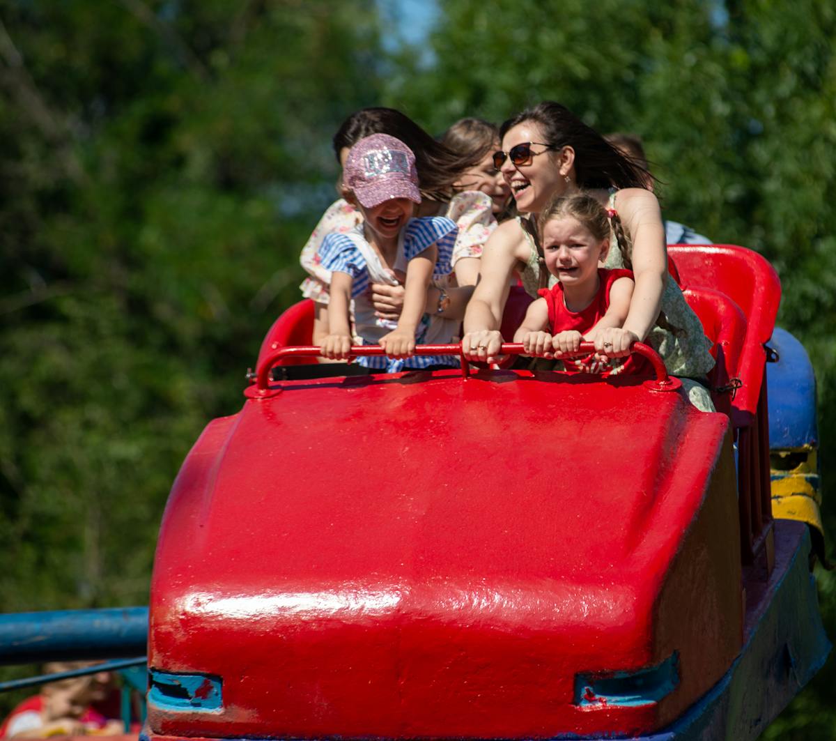 Adults and children riding a red roller coaster at a theme park