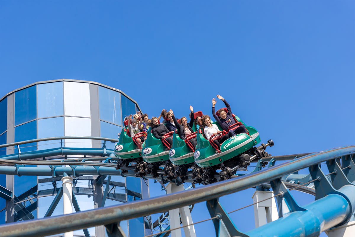 People enjoying a thrilling roller coaster ride at a European theme park under clear blue sky