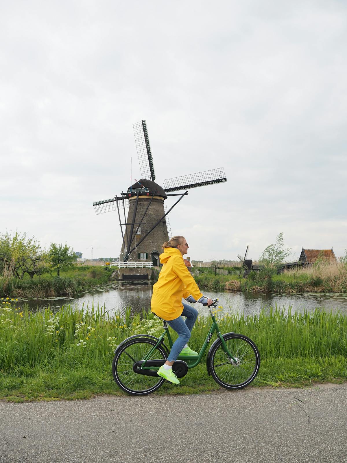 Woman in yellow jacket cycling by a Dutch windmill in spring