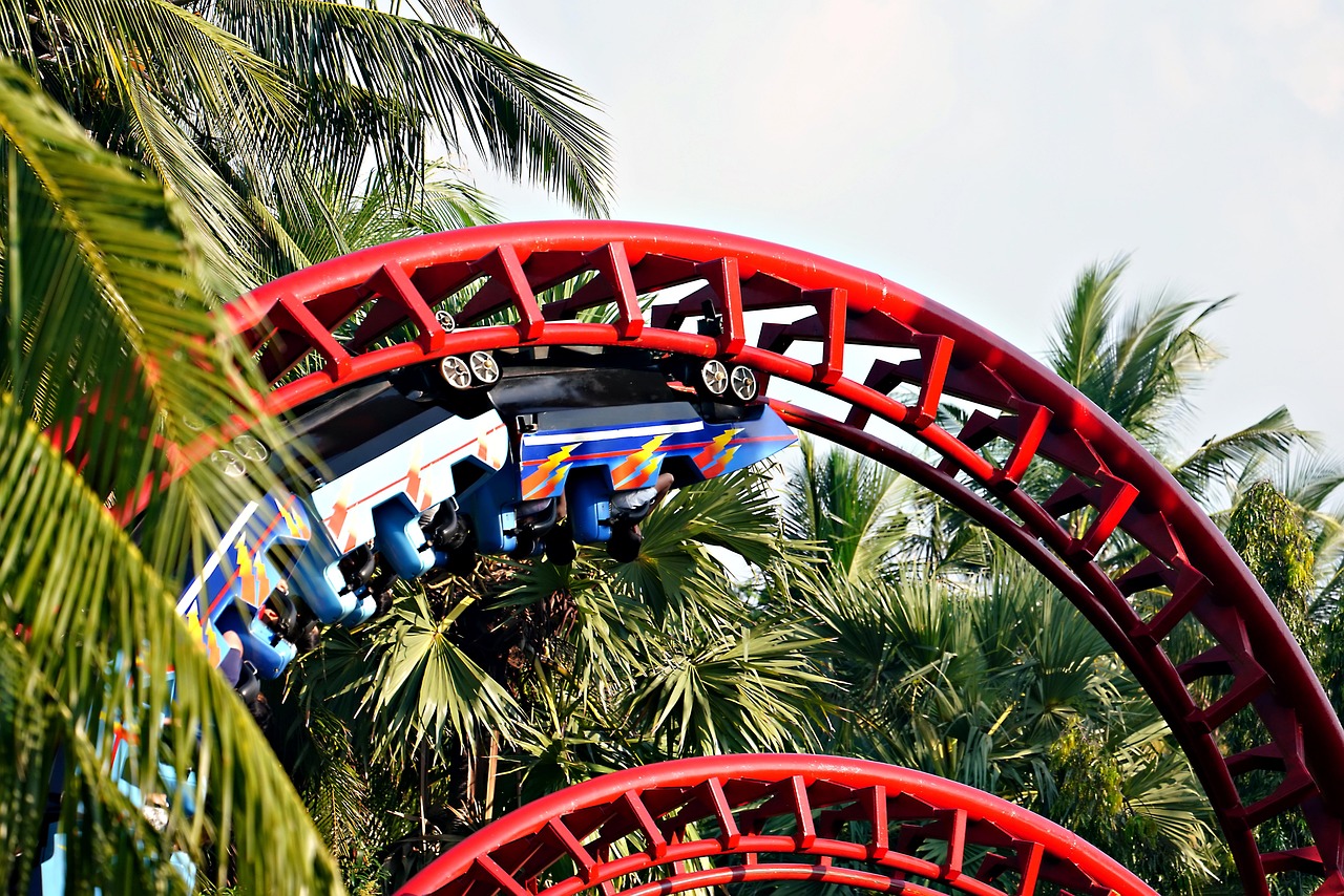 Red roller coaster track winding through palm trees at a theme park