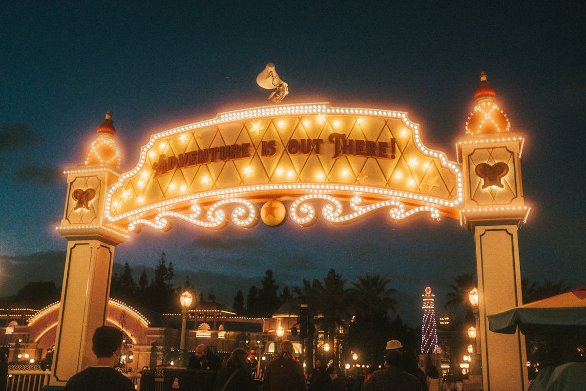 Entrance sign at a theme park glowing with lights during nighttime