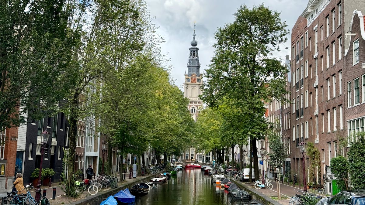 Amsterdam canal lined with bicycles and boats with the Westerkerk church tower in the background