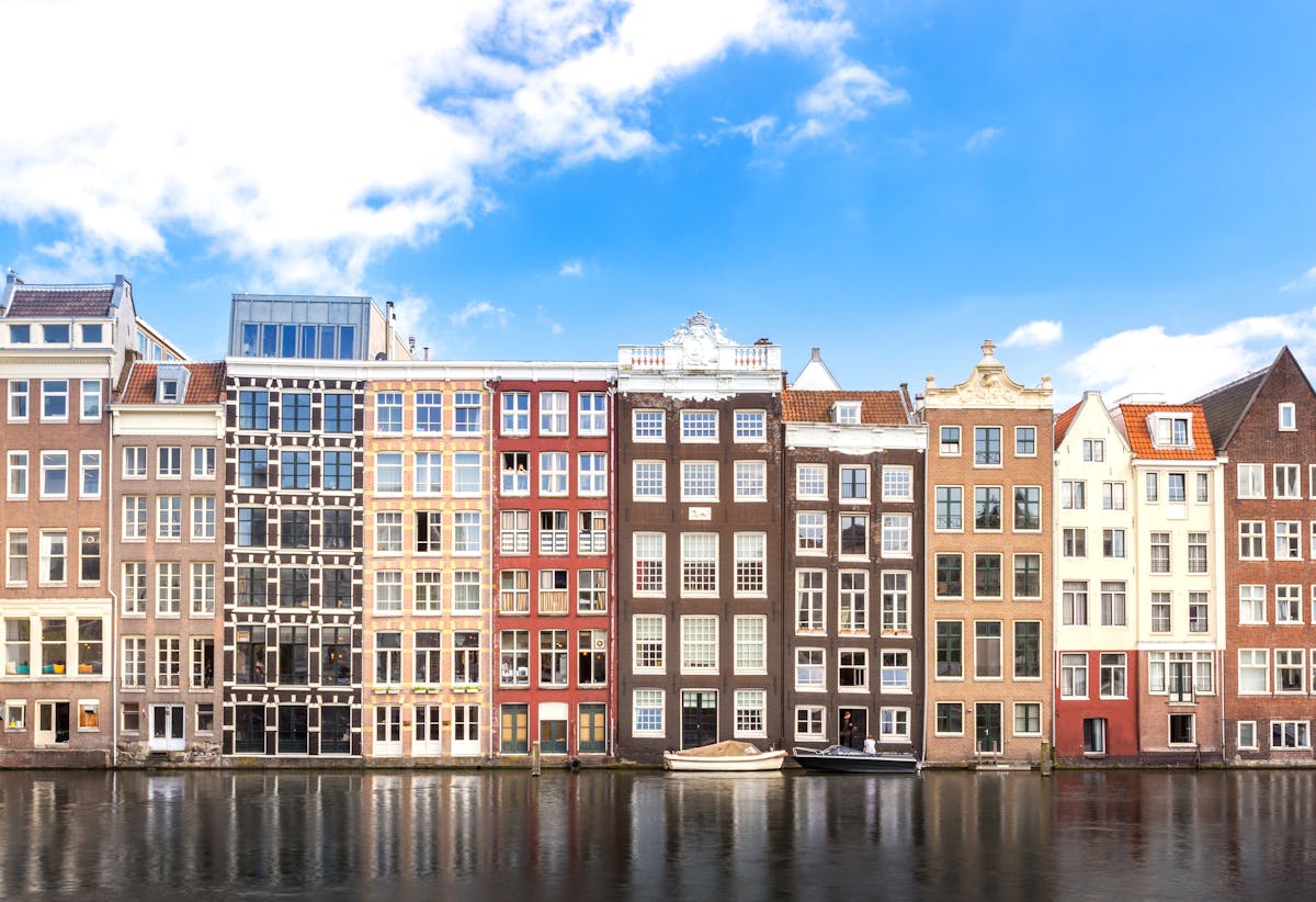 Row of colorful Amsterdam canal houses with reflections in the water under blue sky