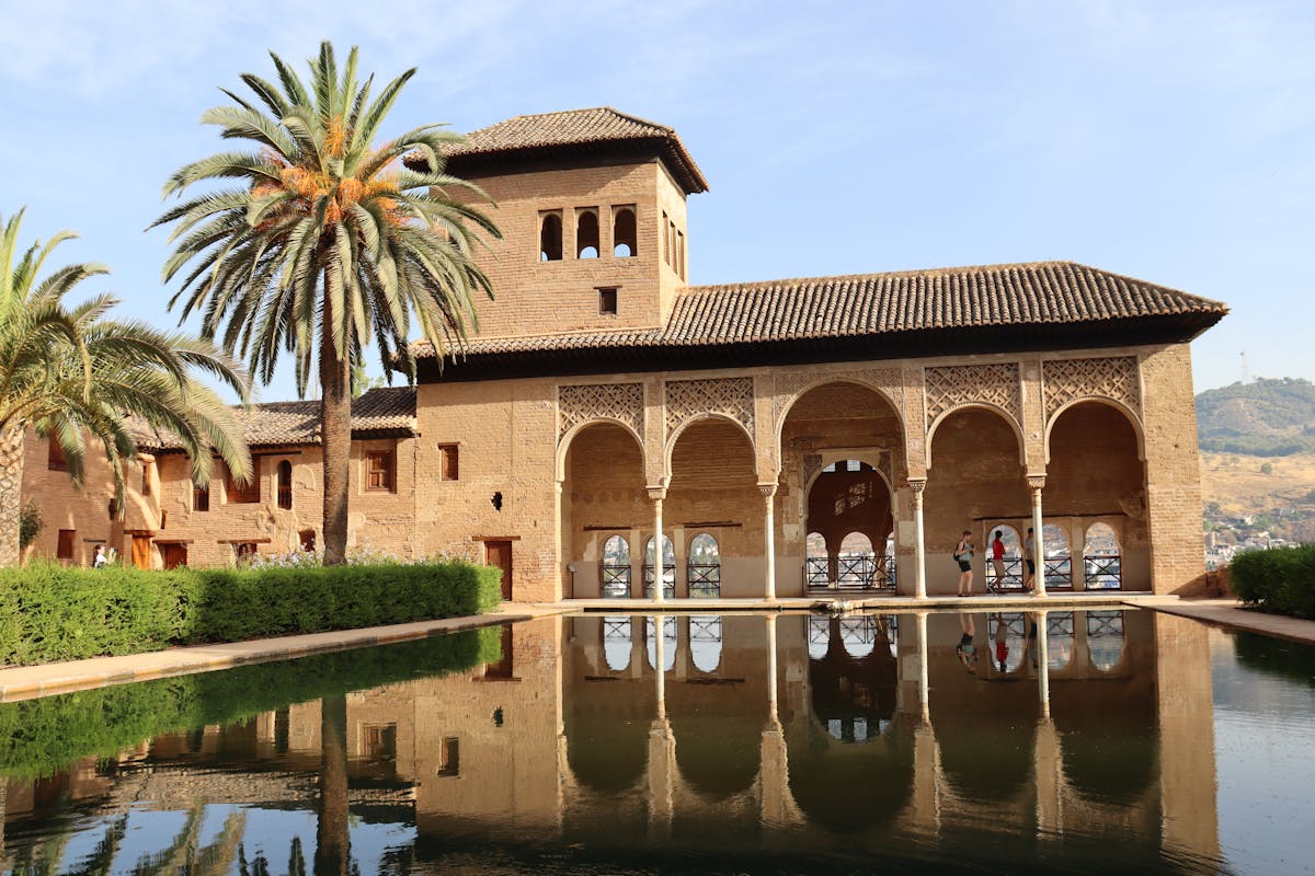 The Alhambra with palm trees and a reflecting pool on a bright day
