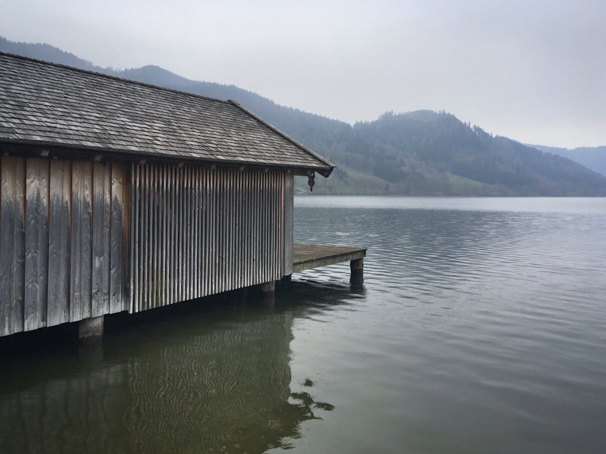 A wooden boathouse on a misty alpine lake in Bavaria with mountains fading into fog