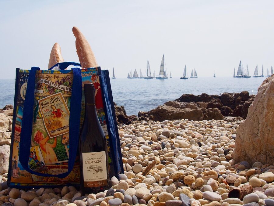 Beach picnic scene with baguette and wine overlooking sailboats in Antibes France