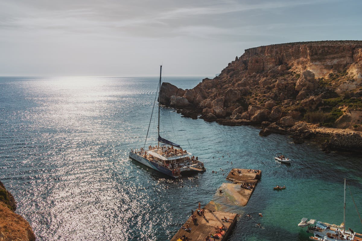 Picturesque coastal bay with yachts and swimmers under warm sun against dramatic limestone cliffs