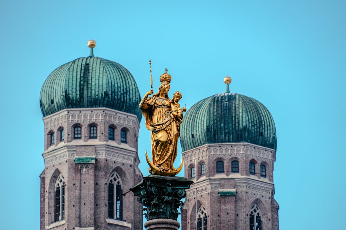 Golden statue of the Virgin Mary at Marienplatz with Frauenkirche twin towers in the background