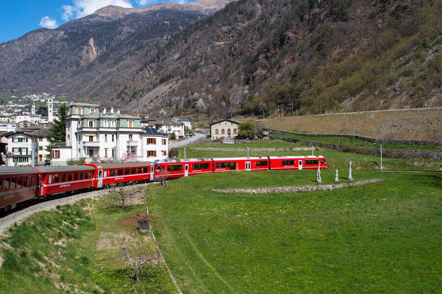 Red Bernina Express train passing through a Swiss Alpine village with snow-capped mountains in the background