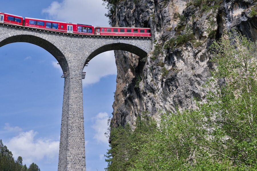 Red train crossing the Landwasser Viaduct in the Swiss Alps surrounded by forest and mountains