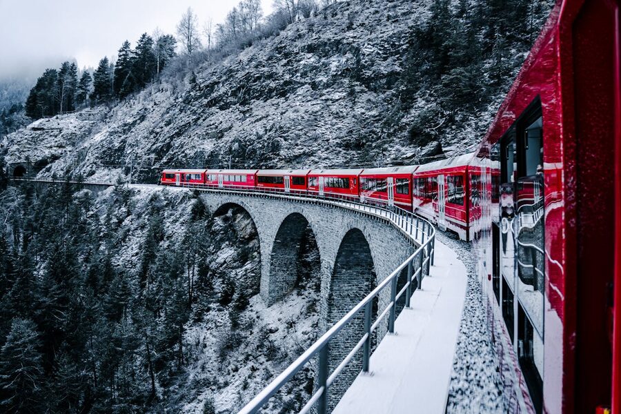 Red train crossing a snow-covered bridge in the Swiss Alps with dramatic mountain scenery