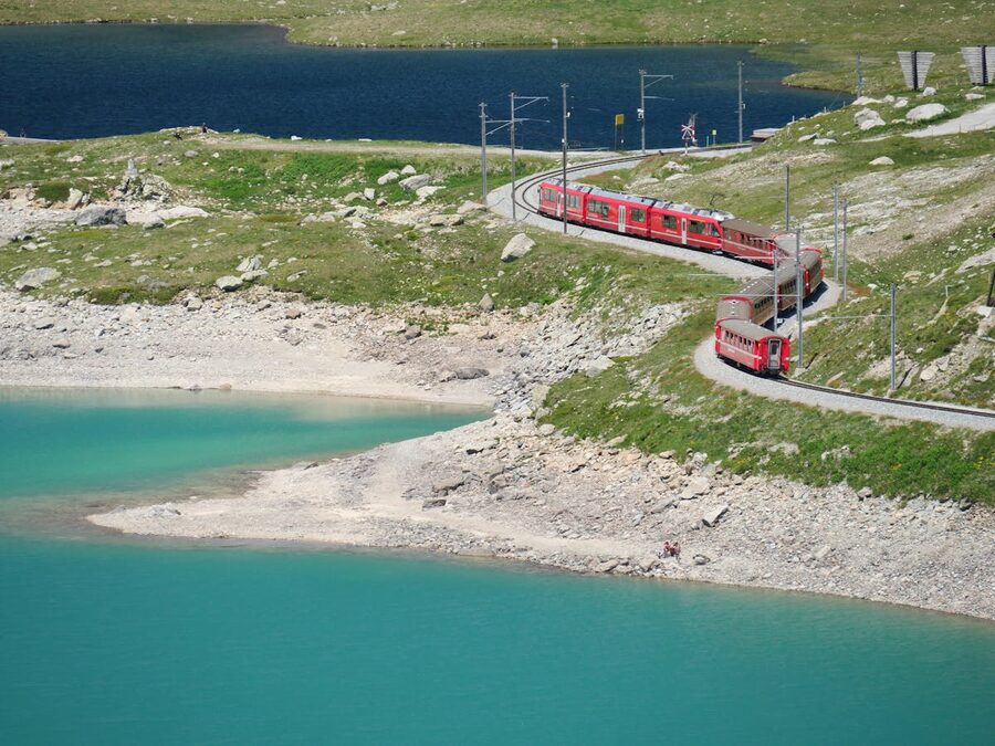 Red Bernina train curving through a green Alpine valley with mountains on all sides