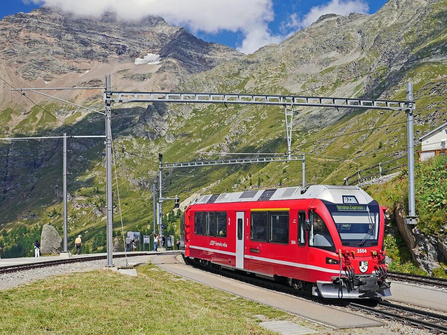 Bernina Express at Alp Grum station with mountain valley view