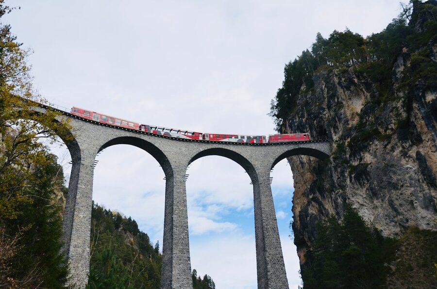 Red train crossing the iconic Landwasser Viaduct with forested Swiss Alps and blue sky
