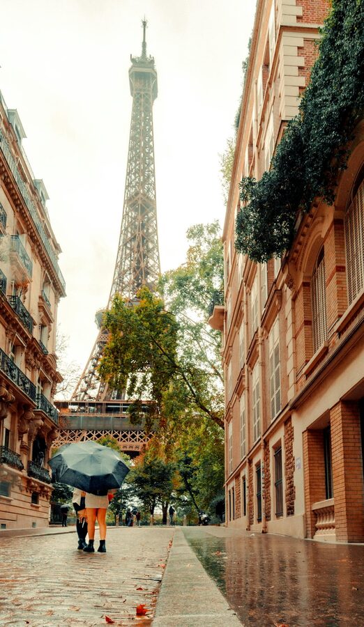 Couple walking along a cobblestone street in Paris with the Eiffel Tower visible in the distance