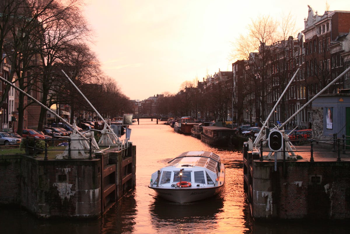 Canal boat navigating Amsterdam canals at sunset with classic architecture