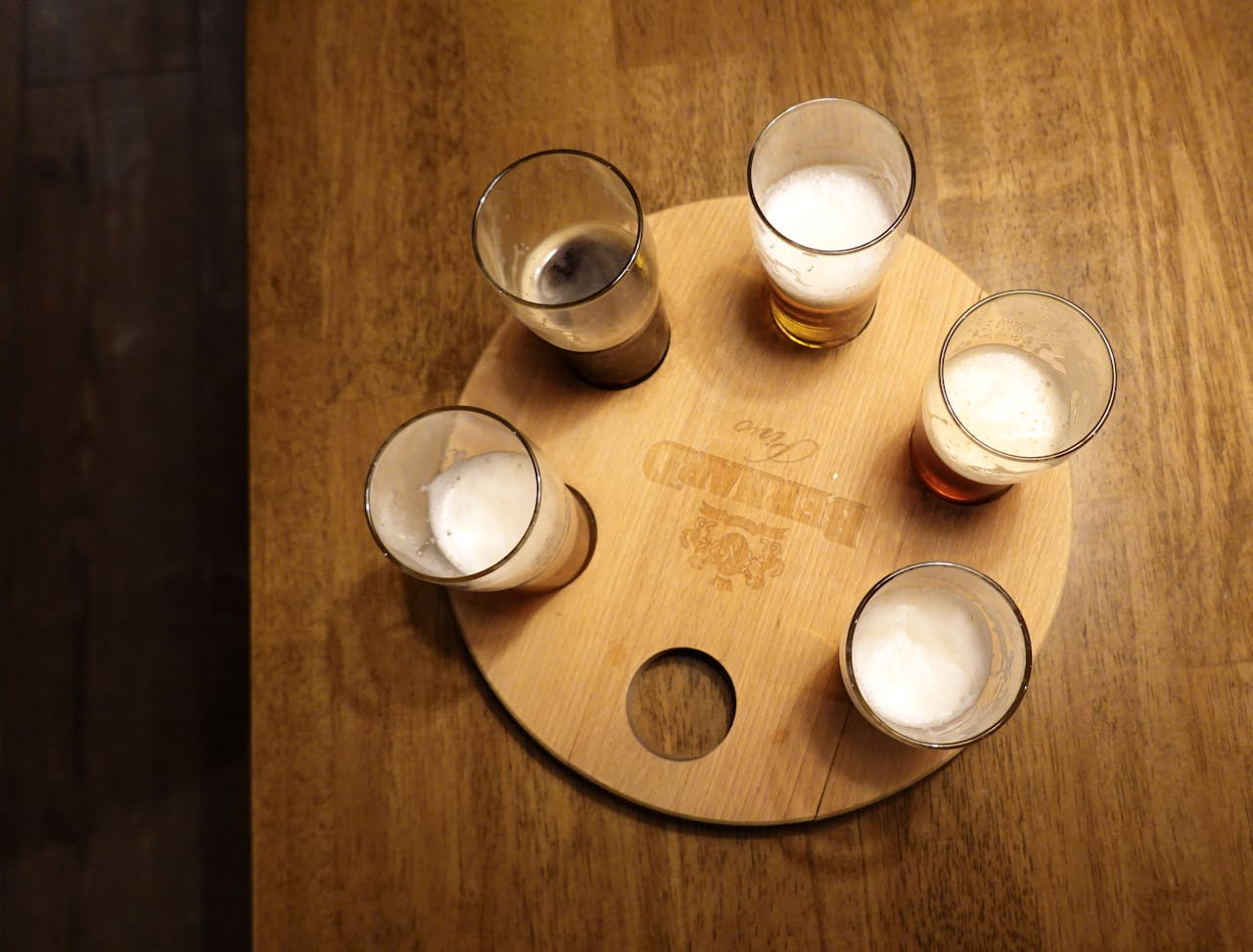 Five glasses of beer with foam on a round wooden tray