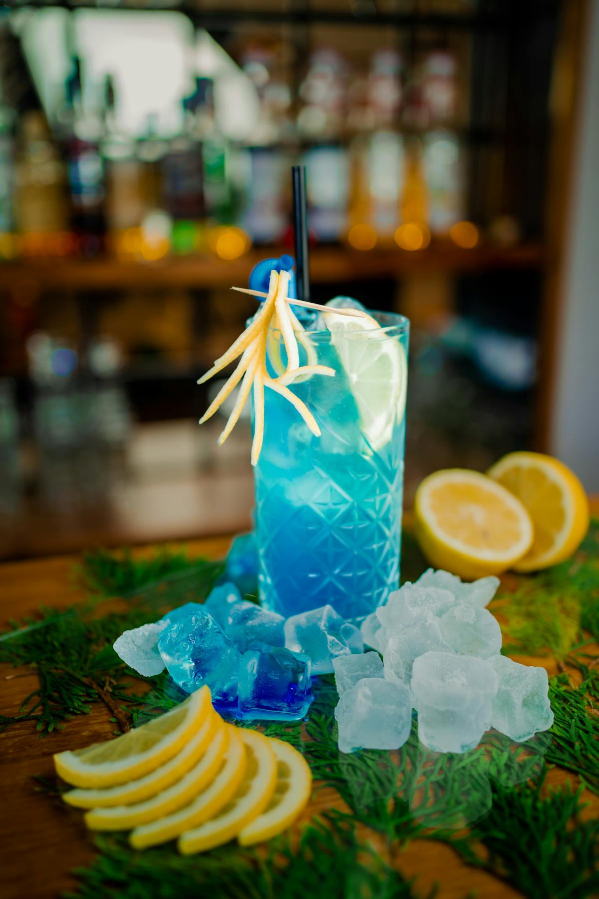 A blue cocktail with lemon slices and ice cubes at a bar