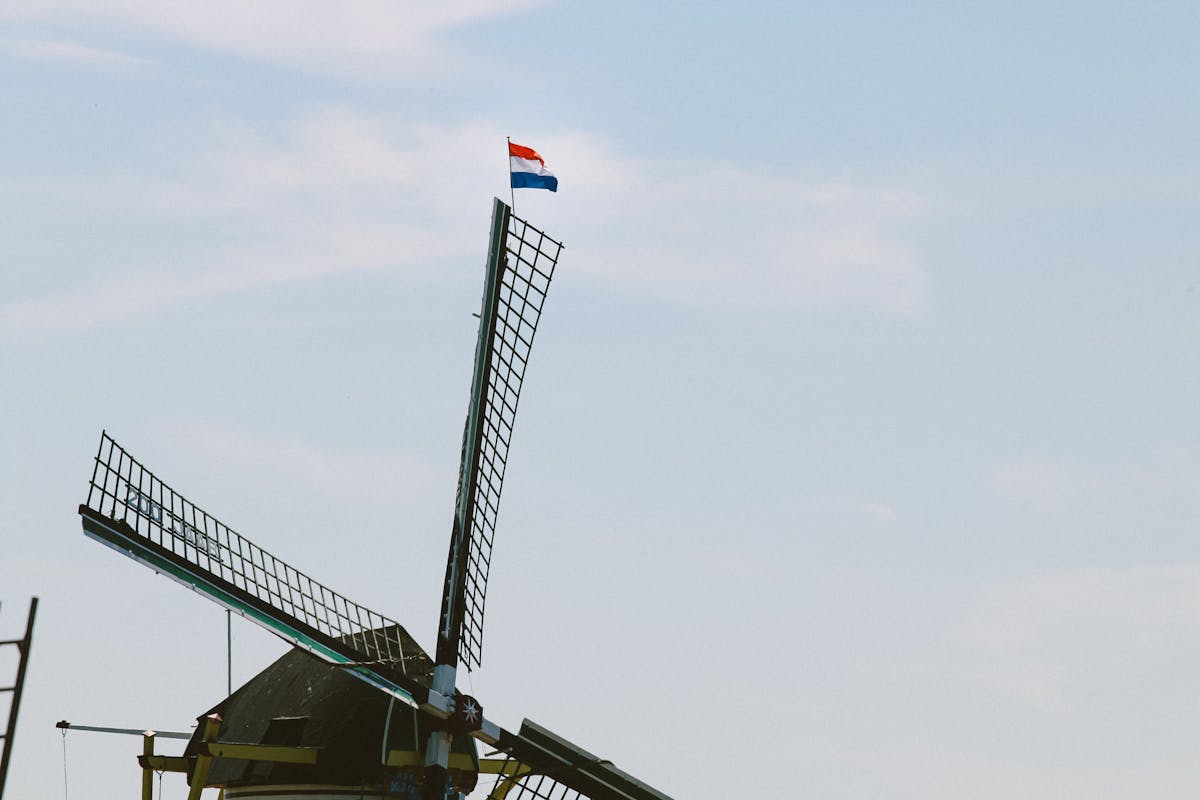 A classic Dutch windmill adorned with the Netherlands flag against a bright blue sky