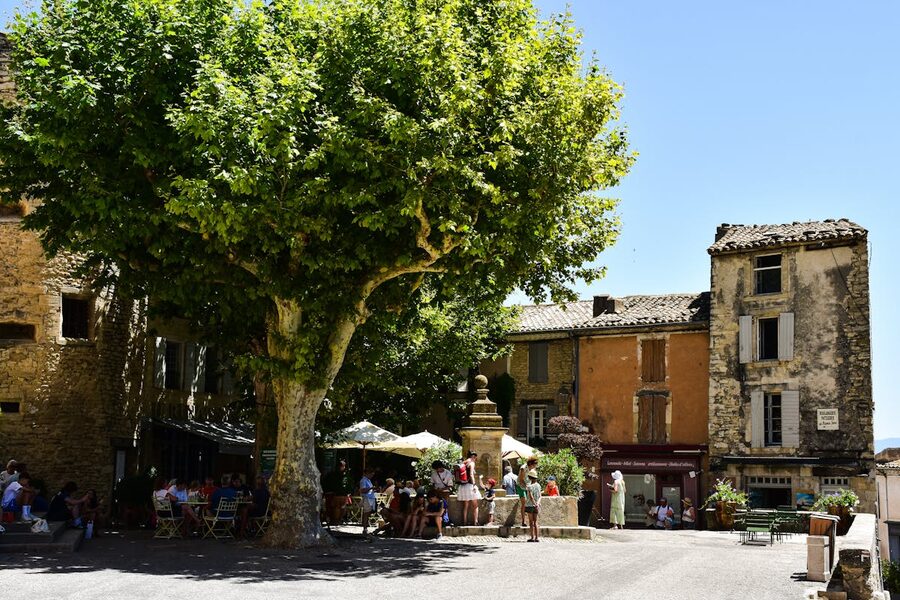 Village square with cafe seating under a large tree in Provence France