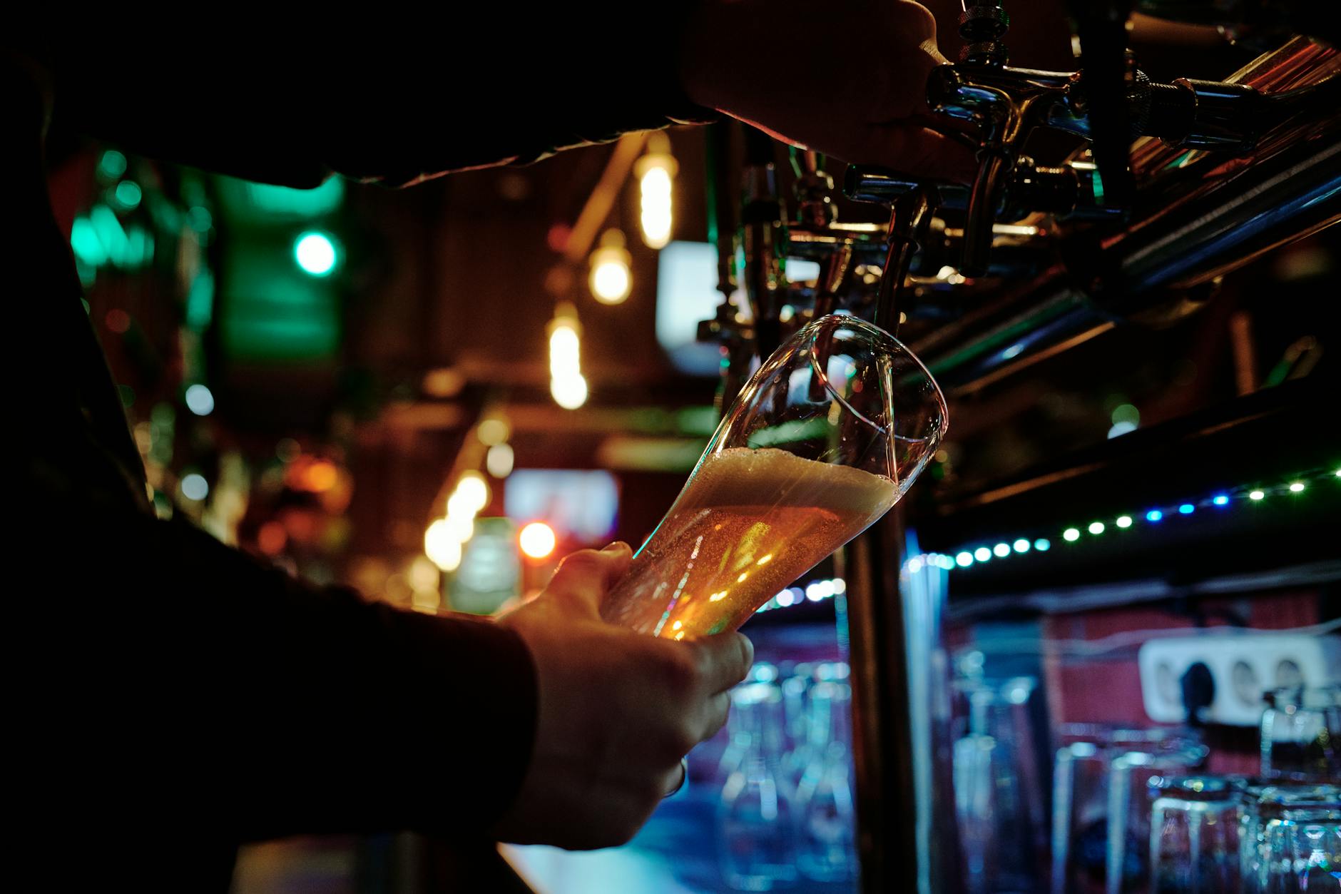 Person pouring beer from a tap at a bar in dim lighting