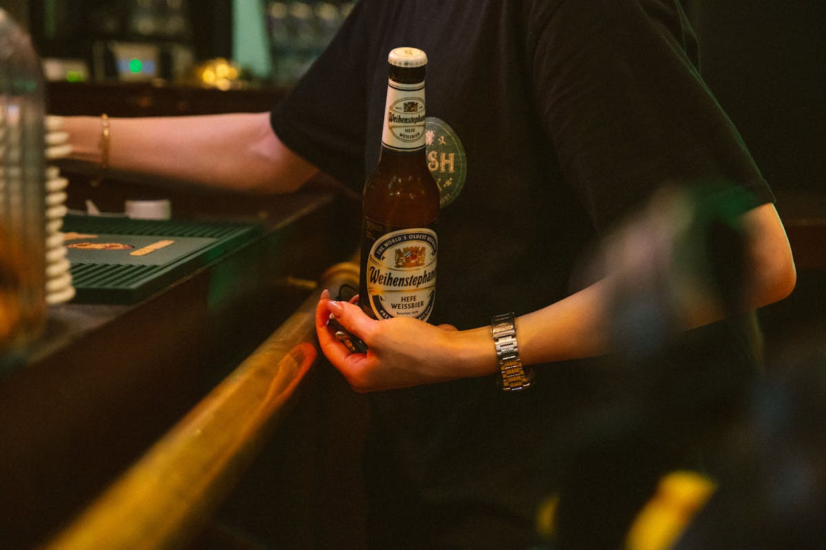 A bartender holds a Weihenstephaner Hefe Weissbier bottle in a pub