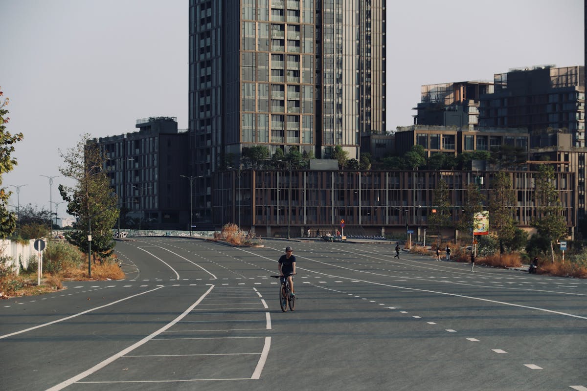 A lone cyclist riding on an empty city street surrounded by modern buildings