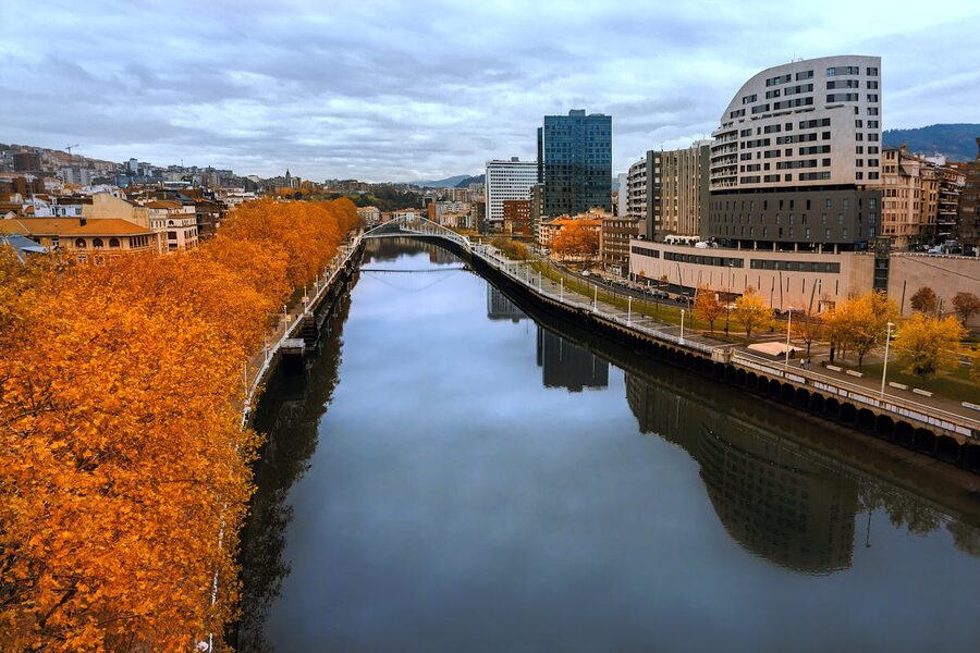Autumn view of a river in Bilbao with orange foliage and modern skyline