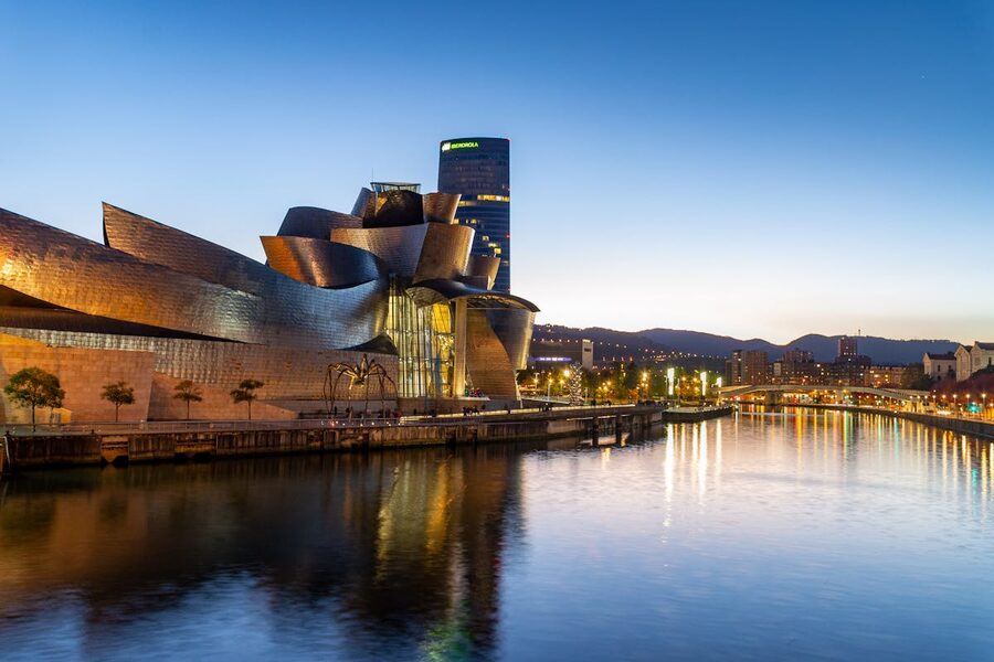 The titanium panels of the Guggenheim Museum reflecting golden light in the Nervion river at sunset in Bilbao