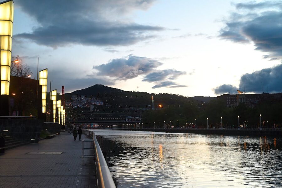 The illuminated riverfront buildings of Bilbao reflected in the Nervion river on a calm evening