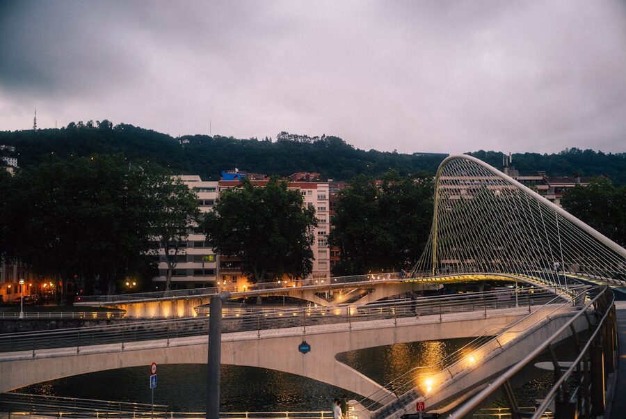 The modern white Zubizuri Bridge in Bilbao lit up at dusk with city lights reflecting in the water